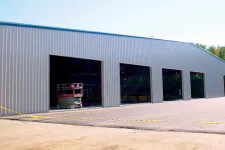 Thumbnail for Large metal warehouse with multiple open bays under clear sky and surrounding green trees.