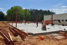 Thumbnail for Construction site with steel beams and concrete foundation amid trees and workers under blue sky.