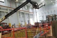 Thumbnail for Indoor construction site with a crane lifting materials over a foundation pit surrounded by safety railings.