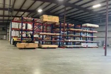 Thumbnail for Warehouse interior with steel racks holding wooden planks and plywood sheets under fluorescent lights.
