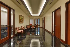 Thumbnail for Modern hallway with glossy black tile floor, wooden doors, beige walls, chairs, and recessed ceiling lights.