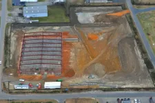 Thumbnail for Aerial view of a construction site with steel framework erected and cleared land around it on a sunny day