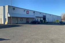Thumbnail for Large industrial warehouse with metal siding under clear blue sky and a parked black car outside.