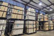 Thumbnail for Wood panels and lumber stacked on tall metal racks in a spacious warehouse with concrete floors and high ceilings.