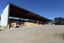 Thumbnail for Covered outdoor storage facility with stacked lumber and a forklift operator under clear blue sky.