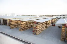 Thumbnail for Outdoor lumber yard with organized stacks of wooden planks under white canopies and a forklift in use.