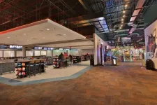 Thumbnail for Spacious modern bowling alley with seating area, bowling balls, and arcade games under industrial ceiling.