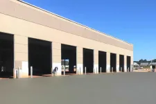 Thumbnail for Exterior of a large industrial warehouse building with multiple wide open loading dock doors under a clear blue sky.