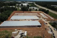 Thumbnail for Aerial view of a large industrial warehouse construction site with metal roofs and surrounding cleared land.