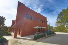 Thumbnail for Two-story red brick building with outdoor seating umbrellas and tables under a partly cloudy sky.