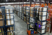 Thumbnail for Forklift operator moving stacked boxes in a large organized warehouse with tall metal shelving units.