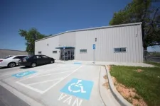Thumbnail for Accessible parking spaces in front of a modern industrial building with cars and clear blue sky.