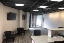 Thumbnail for Modern office reception area with seating, mounted TVs, granite countertop, and wood flooring under black grid ceiling.