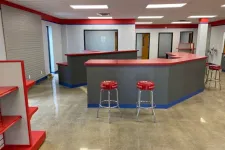 Thumbnail for Modern commercial space with red and gray counters, stools, shelving, and polished concrete floor.