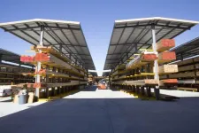 Thumbnail for Outdoor lumber yard with organized stacks of wood under metal canopies and a forklift in the center aisle.