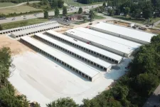 Thumbnail for Aerial view of a large storage facility with multiple long white-roofed buildings surrounded by trees and roads.