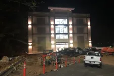 Thumbnail for Illuminated building under construction at night with parked trucks and construction equipment.