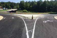 Thumbnail for Freshly paved road with new white lane markings and a traffic cone at a fork under clear skies with trees.