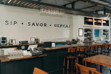 Thumbnail for Modern bar interior with wooden stools, wine glasses, and wall text reading SIP SAVOR REPEAT above counter.