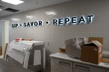 Thumbnail for Illuminated SIP SAVOR REPEAT sign on tiled wall in room with covered furniture and unpacked boxes.