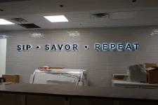 Thumbnail for Illuminated wall sign reading SIP SAVOR REPEAT above a counter in a modern unfinished interior space.