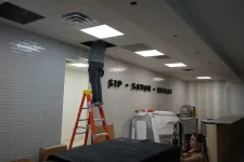 Thumbnail for Worker on ladder installing ceiling tiles in a room with tiled walls displaying 'SIP SAVOR RELAX' sign.