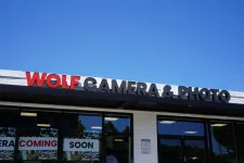 Thumbnail for Storefront of Wolf Camera & Photo with a clear blue sky and Coming Soon signs in the windows.