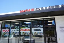 Thumbnail for Storefront with signs in windows announcing Wolf Camera coming soon under a clear blue sky.