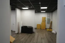 Thumbnail for Empty room with white walls, black ceiling tiles, wooden floor, packed boxes, and electrical panel on the wall.