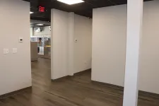 Thumbnail for Empty modern office space with wood-look flooring, white walls, and a ceiling with black tiles and exit sign.