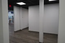 Thumbnail for Empty office space with gray walls, wood flooring, and black tiled ceiling with exit sign.