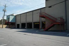 Thumbnail for Empty industrial parking lot next to a beige warehouse with red exterior staircases under a blue sky.