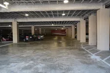 Thumbnail for Indoor parking garage with several parked cars, concrete pillars, and directional signage to upper level shops.