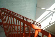 Thumbnail for Sunlit red metal stair railing in an industrial building with light blue and white painted brick walls.