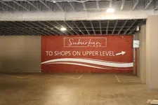 Thumbnail for Red wall sign indicating shops are on the upper level in a parking garage with concrete ceiling.