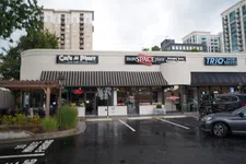 Thumbnail for Storefronts of Cafe A Pharr, moreSPACEplace, and TRIO Shoe Service in an urban shopping plaza with parked cars.