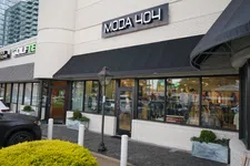 Thumbnail for Street view of Moda 404 fashion store with large windows, black awning, and clothing displays inside.