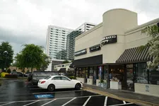 Thumbnail for White car parked outside a brick strip mall with businesses including a nail and spa salon on a cloudy day