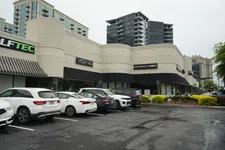 Thumbnail for Shopping plaza with parked cars and stores including MODA 404 and Everything But Water under cloudy sky.