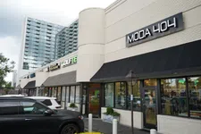 Thumbnail for Street view of modern retail shops with Moda 404 and other store signs under a cloudy sky.