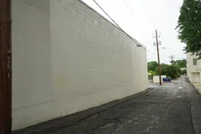 Thumbnail for Empty urban alley beside a plain gray wall with cracked asphalt and power poles under overcast sky