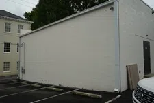 Thumbnail for Empty parking spaces beside a plain white brick building with a black door on an overcast day.