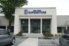 Thumbnail for Exterior view of PGA TOUR Superstore with parked cars and trees under a cloudy sky.