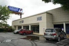 Thumbnail for Storefront with signs for lessons, repairs, and fittings beside a parking lot with three cars and a justice billboard above.