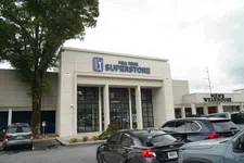 Thumbnail for Exterior view of PGA Tour Superstore with parked cars and Men's Wearhouse store beside it on cloudy day
