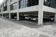 Thumbnail for Cars parked under a modern office building with large windows and a cracked asphalt driveway.