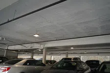Thumbnail for Indoor parking lot with multiple cars parked under a concrete ceiling with overhead lights and pipes.