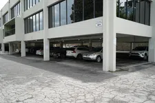 Thumbnail for Covered parking lot under an office building with various cars parked and cracked asphalt pavement