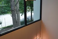 Thumbnail for Modern geometric pendant lights and sconces illuminate a stairwell with large windows and green trees outside.