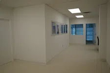 Thumbnail for Bright office hallway with white walls, ceiling lights, framed pictures, and a window overlooking urban buildings.
